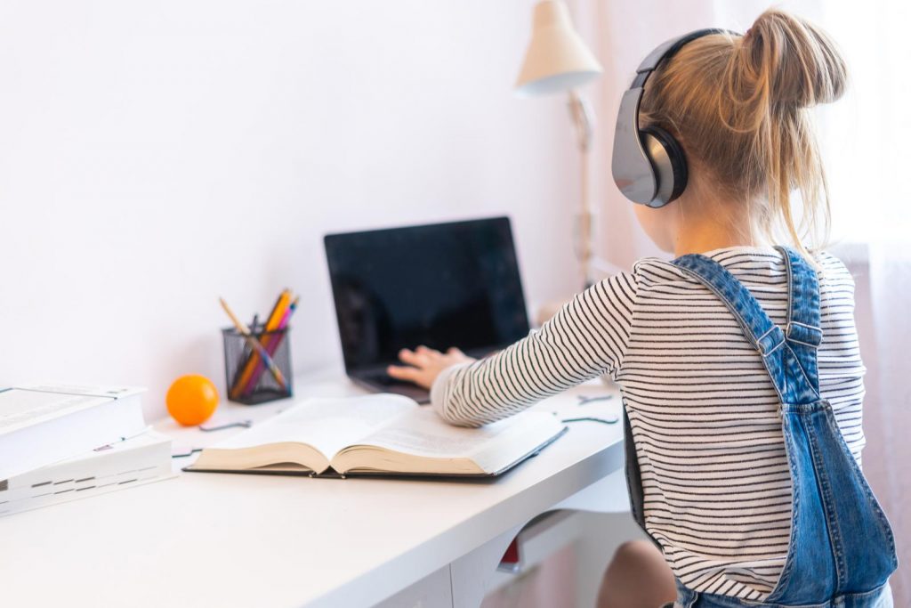 preteen girl doing her homework at home and using a laptop